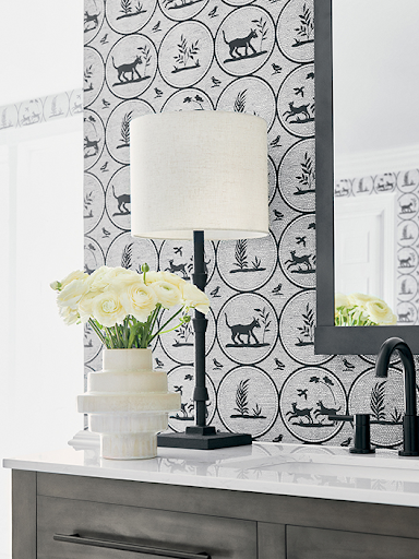 Grey wallpaper with patterns of dogs, birds, and plants line the walls of the a white and grey bathroom counter. 